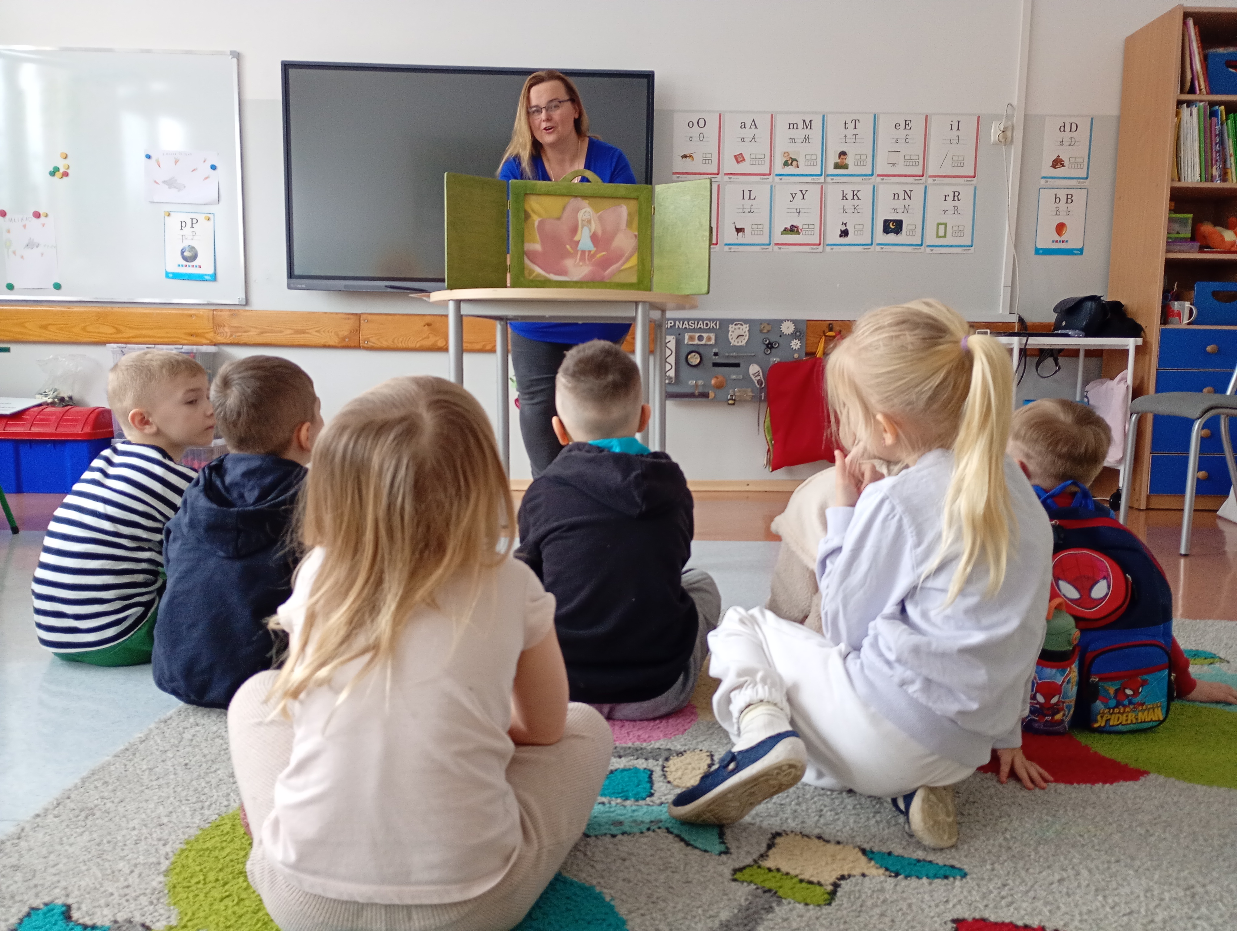 Uczniowie siedzą na&nbsp;dywanie i&nbsp;oglądają teatrzyk.