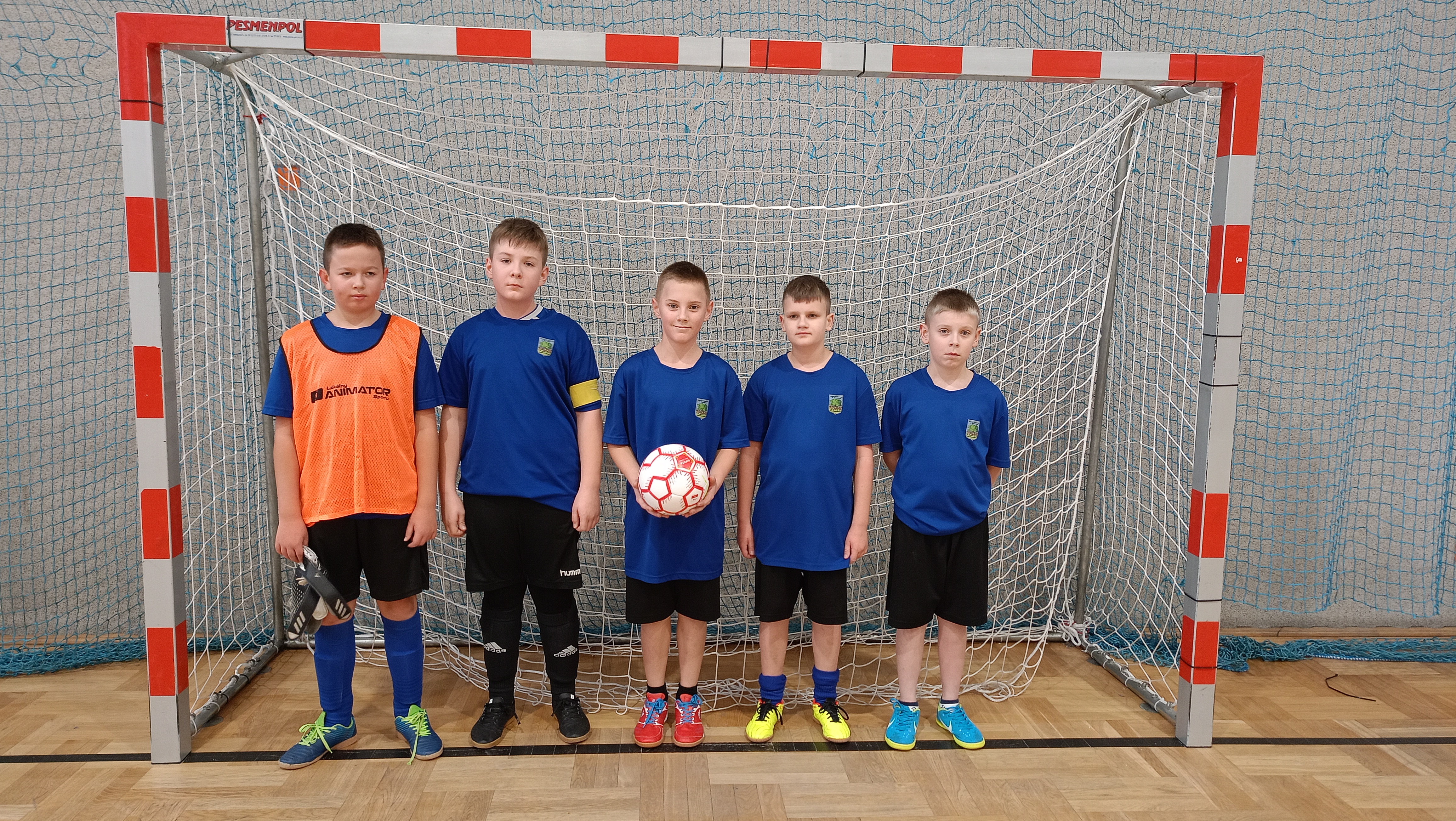 Grupa chłopc&oacute;w w&nbsp;strojach sportowych na&nbsp;tle bramki.