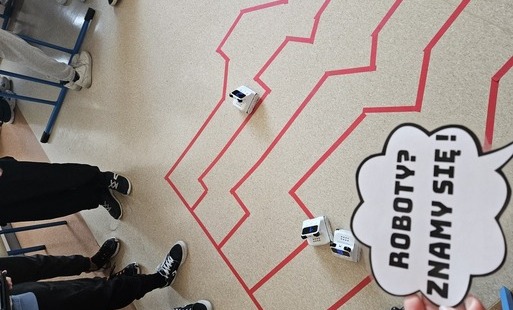 Roboty edukacyjne na trasie wyznaczonej czerwonymi taśmami.