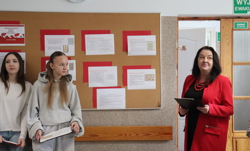 Nauczycielka i uczennice na tle gazetki z okazji Dnia Języka Ojczystego.