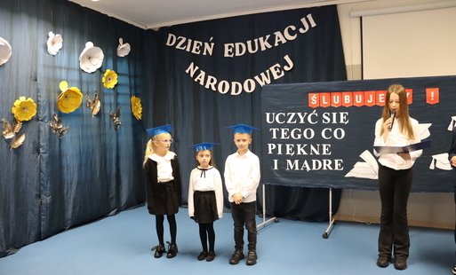 Uczniowie ubrani na galowo, za nimi napis "Dzień Edukacji Narodowej".